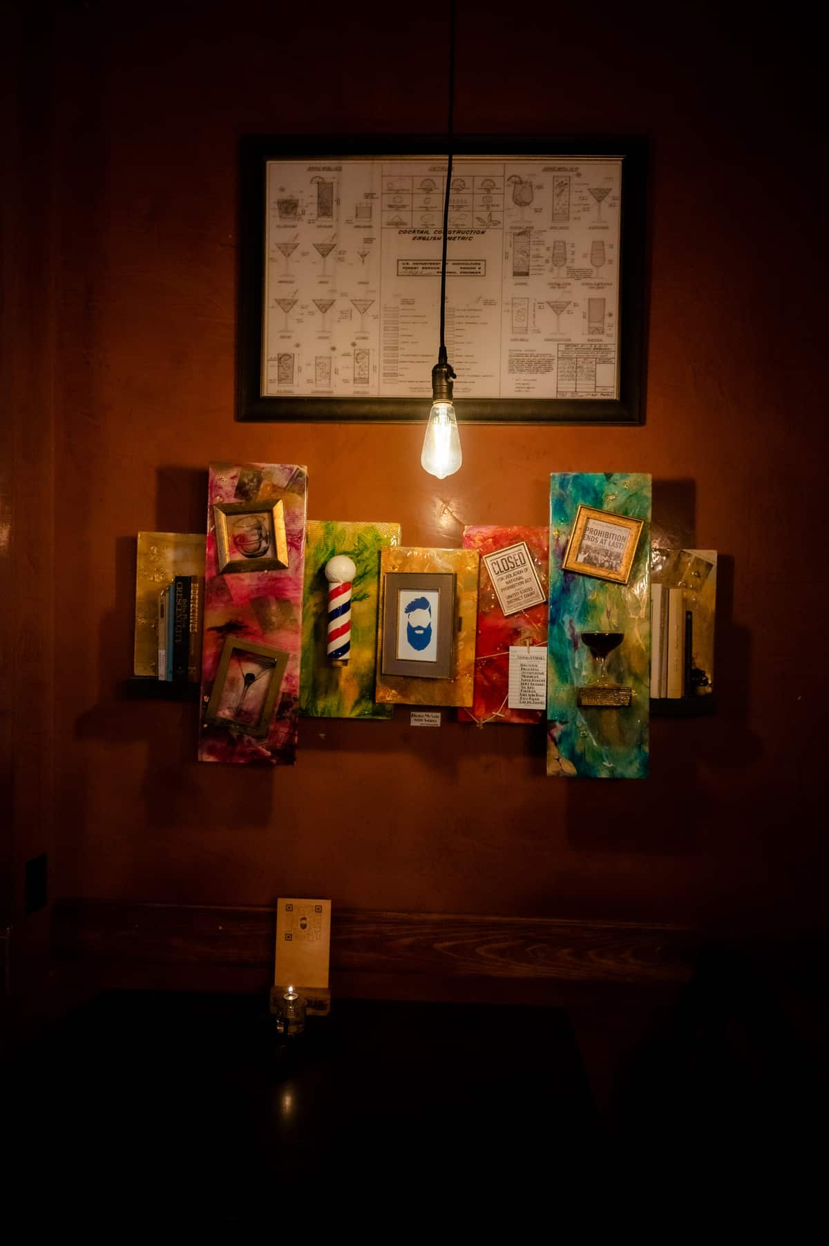 Speakeasy-themed art wall inside the Bookcase — barber pole motif, cocktail blueprints, and Edison bulb